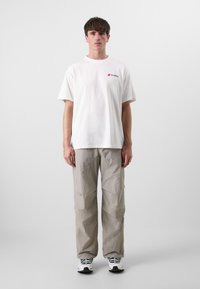 Hvit bomull t-skjorte med en liten rød logo, kombinert med grå, teksturerte, løstsittende bukser og svarte og hvite sneakers.