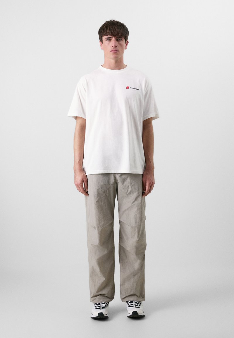 Hvit bomull t-skjorte med en liten rød logo, kombinert med grå, teksturerte, løstsittende bukser og svarte og hvite sneakers.
