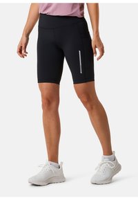 Sorte træningsshorts med høj talje, der har en sidelomme og en reflekterende stribe. Båret med hvide sneakers.