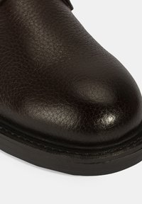 Bruine leren schoen met een gematteerde afwerking, glanzend oppervlak, afgeronde vorm en een contrasterende zwarte rubberen zool. Gevoegde details zichtbaar.