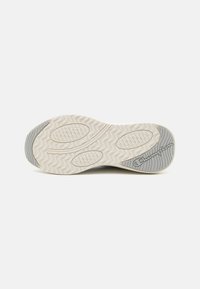 Semelle extérieure en caoutchouc blanc texturé avec un motif ondulé, accents gris et détails circulaires en relief. Présente le logo sur le côté latéral pour le branding.
