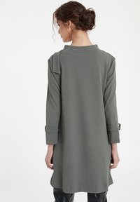 Gray long-sleeve dress with a relaxed fit, roll-up cuff details, and a high neckline. Soft, textured fabric, falling just above the knee.