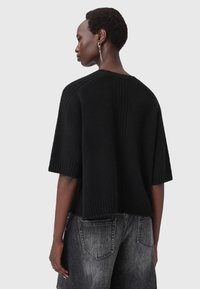 Maglione corto a maniche corte di colore nero in maglia con texture a costine e vestibilità rilassata. I dettagli includono un ampio scollo e una lunghezza leggermente cropped.