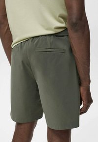 Shorts vert foncé avec une texture lisse, dotés de deux poches arrière avec rabats. Taille élastique pour le confort, visible d'un angle arrière.