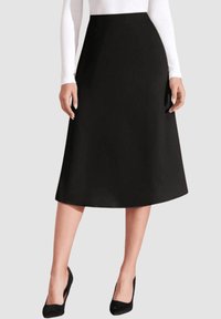 Falda negra en línea A con una textura suave, corte midi y cintura alta. Llevada con una blusa blanca de manga larga y tacones altos negros.