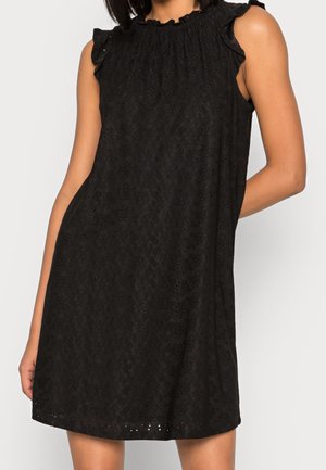 Czarna sukienka bez rękawów z delikatnym kwiatowym wzorem ażurowym i marszczonym dekoltem, noszona przez modelkę z jedną ręką zgiętą za plecami.