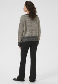 Grijze en beige gebreide trui met een textuurpatroon, ronde halslijn en boorden met ribbels, gecombineerd met zwarte flared broek en platte schoenen.