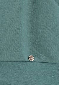 Un tessuto in cotone misto color turchese presenta una superficie testurizzata, con un'etichetta metallica circolare vicino all'orlo inferiore, incisa con "Key Largo."