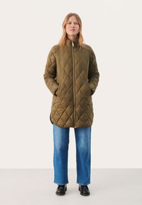Gestepptes olivgrünes Jackett mit hohem Kragen, Reißverschluss und seitlichen Taschen, kombiniert mit gerade geschnittenen blauen Jeans und schwarzen Stiefeln.
