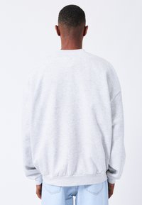 Sudadera gris claro con un corte relajado, puños y cinturilla acanalados. Tela suave con una textura lisa y hombros caídos.