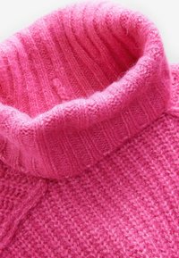 Roosa kudumiga pullover, millel on soonikkoes kõrge kaelus, esitleb tekstureeritud mustrit ja pehmet, karvast lõnga. Kere osas on kudumisdisain.