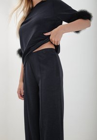 Zwarte textuur top met vachten accenten op de mouwen, gecombineerd met losse zwarte broek met knoopdetail en zijzakken.