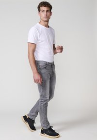 Šedé skinny džíny, bílé tričko a černé tenisky. Džíny mají klasický design s pěti kapsami, jemným vyblednutím a švy.