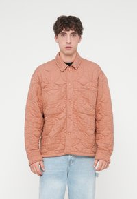 Πανωφόρι με καπιτονέ ύφασμα σε απαλό ροδακινί χρώμα, με γιακά, κουμπιά με κούμπωμα και δύο εμπρόσθιες τσέπες με υφή που μοιάζει με φύλλα.