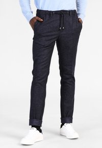 Mörkblå texturerade byxor med ett prickigt mönster, elastisk midja, justerbar dragsko och uppvikta fållar, i kombination med vita sneakers.