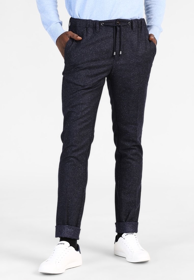 Mörkblå texturerade byxor med ett prickigt mönster, elastisk midja, justerbar dragsko och uppvikta fållar, i kombination med vita sneakers.