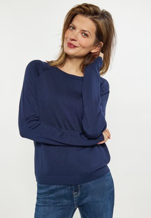 Maglione in maglia blu navy con maniche lunghe e scollatura rotonda, abbinato a jeans blu scuro. Il tessuto sembra morbido e strutturato.