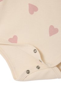 Cream-colored baby bodysuit with light pink heart patterns, featuring press-stud closures at the bottom and soft cotton texture.
