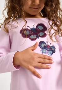 Ροζ πουκάμισο με μακριά μανίκια, διακοσμημένο με μεγάλα σχέδια πεταλούδας με παγέτες σε μπλε, μοβ και ασημί, με διακριτική υφή και λεπτομέρεια.