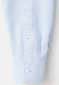 Poignet de chemise bleu clair à manches longues avec un design pointu, doté de deux boutons blancs, une texture lisse et des détails de couture double.