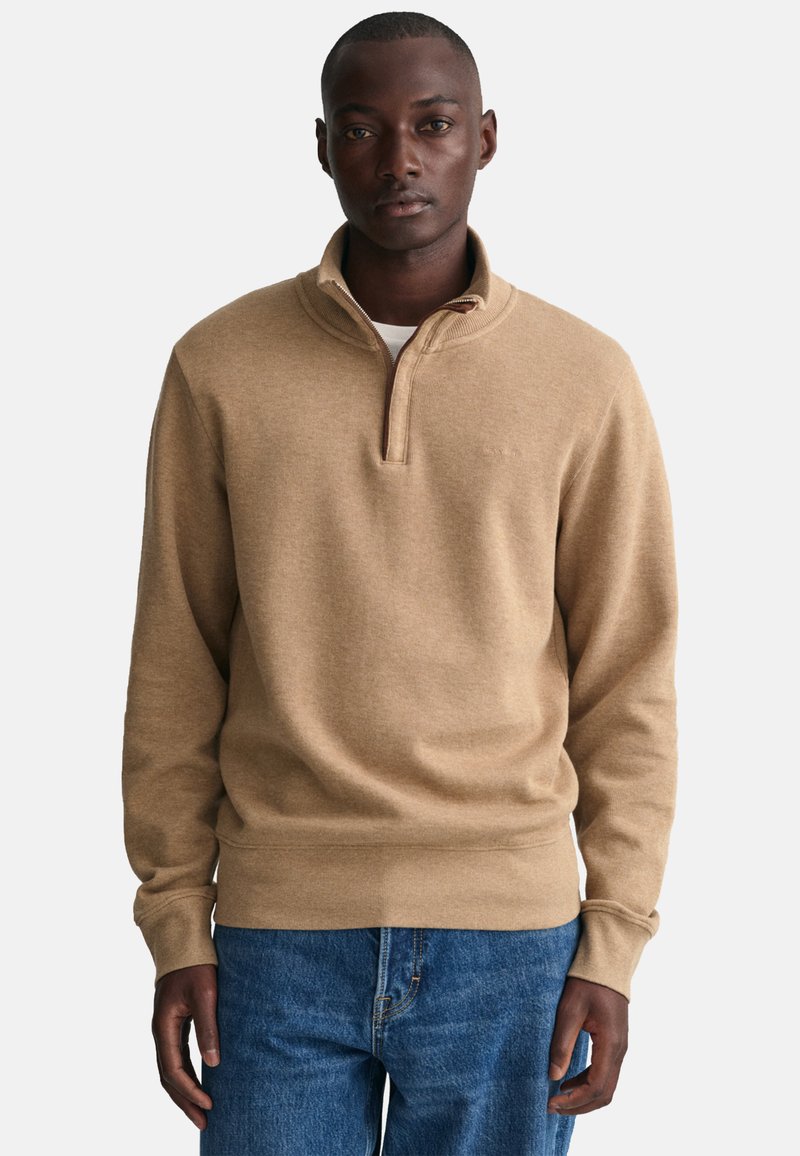 Beige pullover trui met een kwart-rits kraag, geribbelde manchetten en een zachte textuur. Draag het over een wit shirt, in combinatie met blauwe jeans.