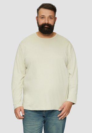 Beige Baumwollhemd mit langen Ärmeln, Rundhalsausschnitt, leichter Textur und geradem Saum. Getragen mit blauen Jeans.