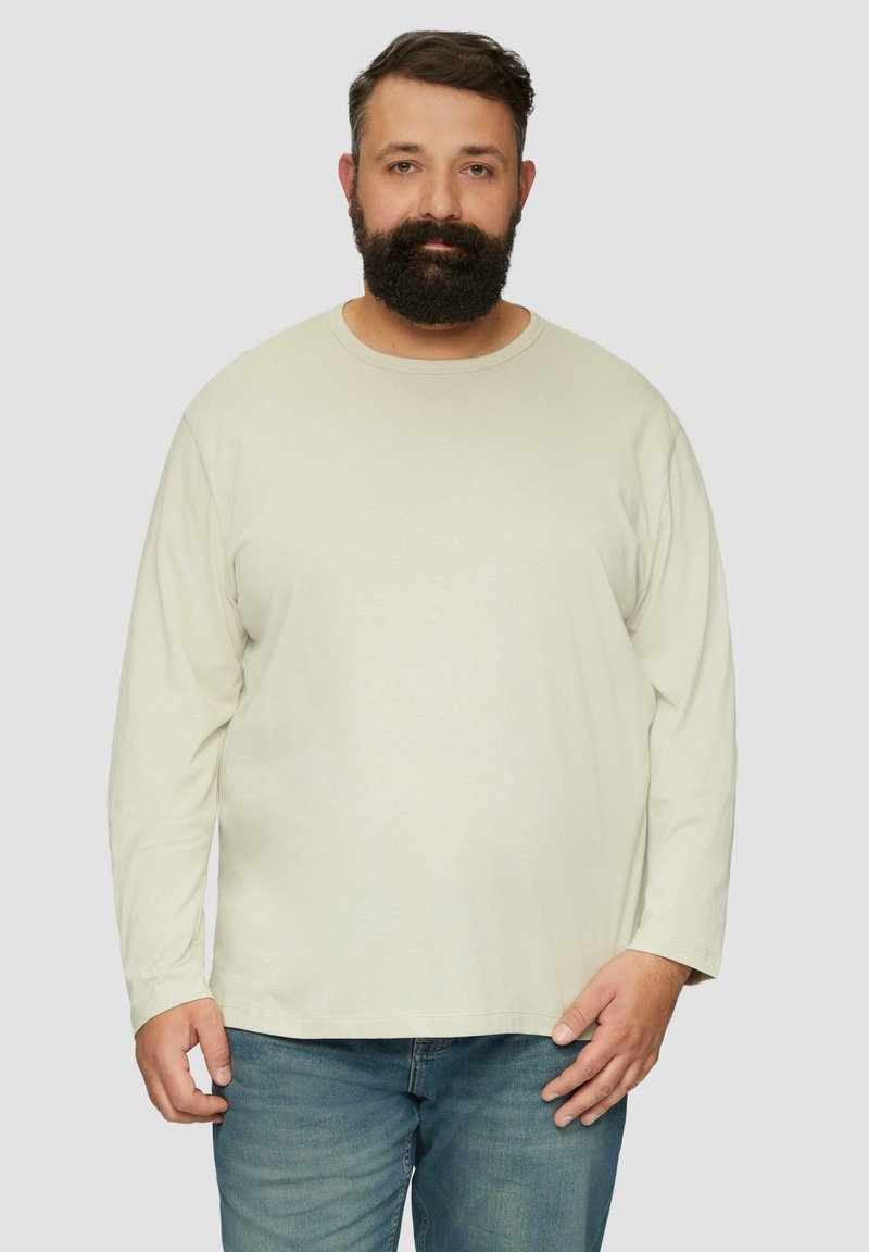 Beige Baumwollhemd mit langen Ärmeln, Rundhalsausschnitt, leichter Textur und geradem Saum. Getragen mit blauen Jeans.
