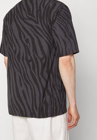 Kortärmad skjorta i mörkgrått tyg med svart zebrarandigt mönster, med avslappnad passform och rak nederkant.