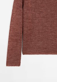 Pull en maille à manches longues de couleur rose poudré avec un ourlet et des poignets côtelés, posé à plat sur fond blanc.