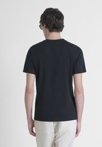 Black cotton t-shirt with short sleeves, classic crew neck, and a smooth texture, worn by a person facing away, paired with light-colored pants.