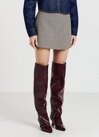 Una corta gonna a quadri abbinata a stivali sopra il ginocchio lucidi color borgogna con punte appuntite e cerniere laterali. La parte superiore è una camicia di jeans.