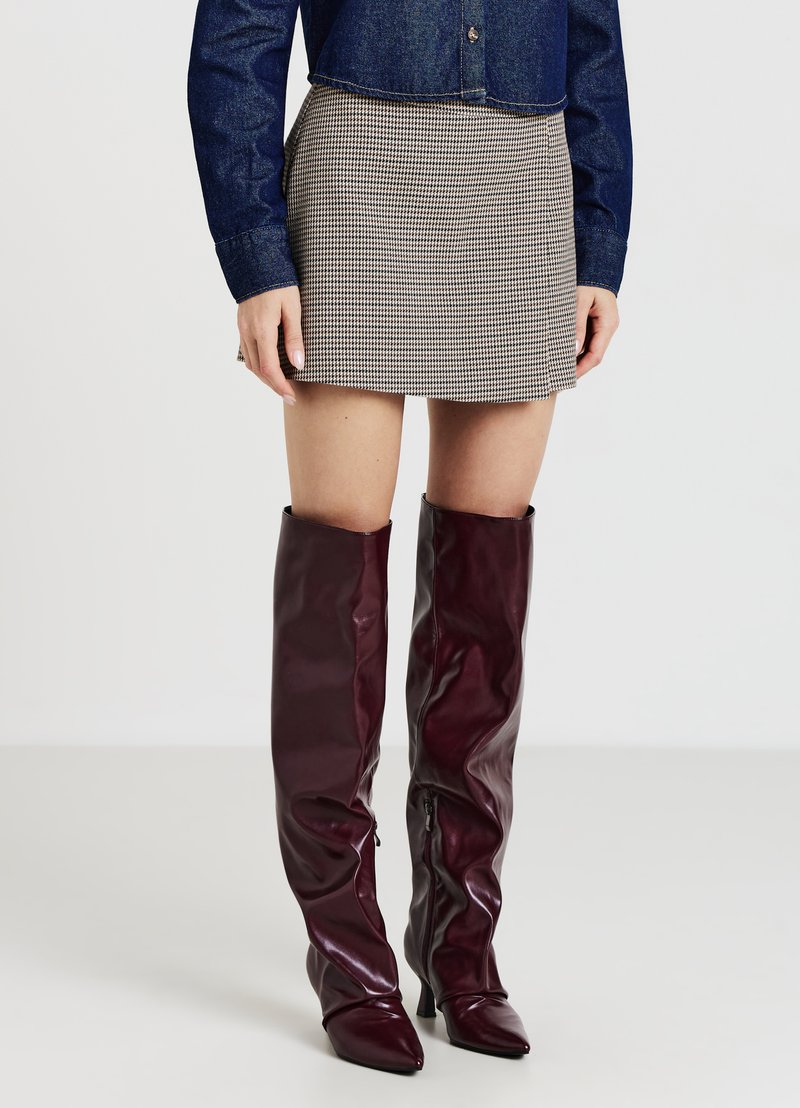 Una corta gonna a quadri abbinata a stivali sopra il ginocchio lucidi color borgogna con punte appuntite e cerniere laterali. La parte superiore è una camicia di jeans.