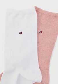 Δύο ζευγάρια κάλτσες: ένα λευκό με ένα μικρό λογότυπο και ένα ροζ με διακριτική υφή. Και τα δύο είναι αστραγάλου μήκους και από απαλό υλικό.