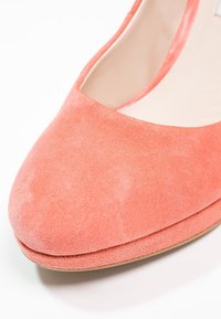 Chaussure de ballet plate en daim rose corail avec bout arrondi et doublure intérieure beige sur fond blanc.
