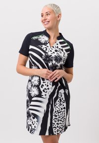 Robe à manches courtes avec un motif floral et animal noir et blanc, décolleté en V et accents verts contrastants sur les épaules.
