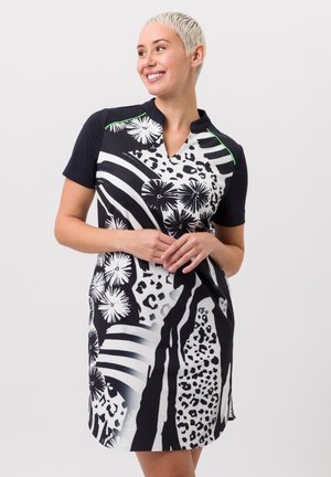Robe à manches courtes avec un motif floral et animal noir et blanc, décolleté en V et accents verts contrastants sur les épaules.