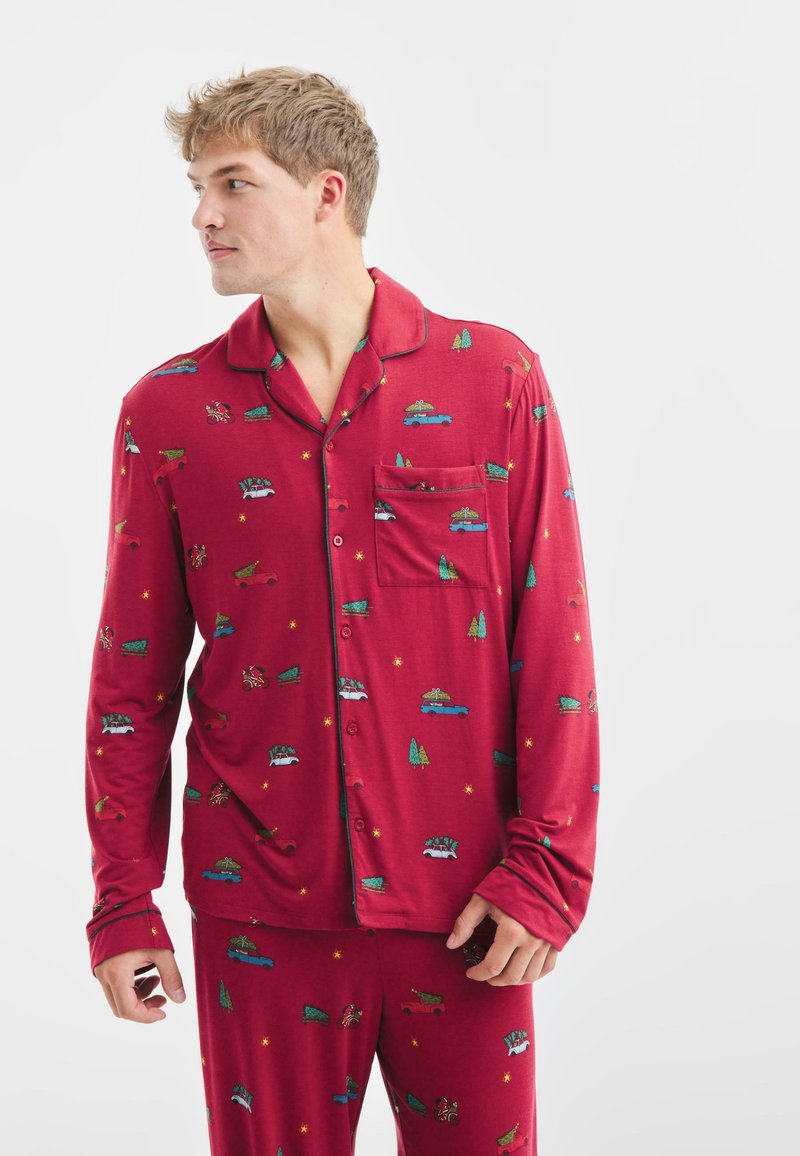 Rode pyjama-set met een witte overhemd met knopen en bijpassende broek. Voorzien van patronen van auto’s, bomen en sterren. Zachte, lichte stof.