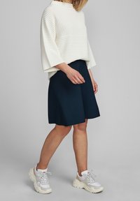 Biały sweter z golfem w prążki z szerokimi rękawami, sparowany z granatową spódnicą dzwonową. Obuwie: masywne białe sneakersy z szarymi akcentami.