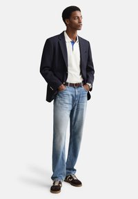 Mornarsko moder blazer preko bele polo majice z modrimi poudarki, svetlo modre kavbojke in rjavi semiš supergi z belimi vezalkami in bež podplati.