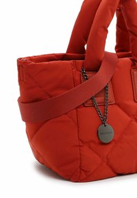 Red quilted handbag with padded texture, dual handles, and a detachable chain featuring a circular tag. Material appears synthetic.