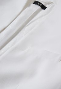 Close-up van de kraag van een wit colbert en borstzak, met een gladde stof en een C&A merklabel aan de binnenkant van de halslijn.