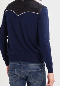 Maglione blu navy con una parte superiore posteriore nera testurizzata, caratterizzato da piping bianco sulle spalle e polsini e orlo a costine.