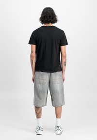 Sort T-shirt med korte ærmer, parret med lysegrå cargo shorts i knælang længde med baglommer og denimstruktur. Hvide sneakers med detaljer.