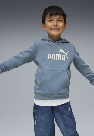 Svetlo modrá mikina s kapucňou a predným vreckom, s bielym logom "PUMA". Nosená cez bielu košeľu s roztrhnutými modrými džínsami.