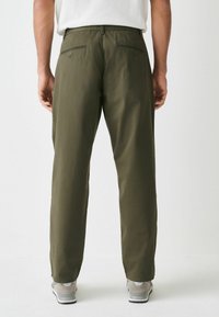 Olive green trousers with a straight leg fit, two back pockets, and a smooth texture, paired with gray sneakers.