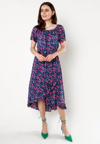 Bloemen midi-jurk in marineblauw met roze bloemen, korte mouwen en een gerimpelde zoom. Gecombineerd met groene sandaaltjes. Lichte stof.