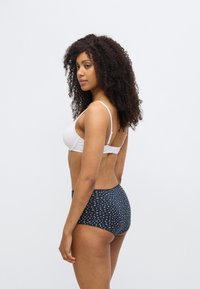 Λευκό στηθόδεσμο με επένδυση και ρυθμιζόμενους ιμάντες, συνδυασμένος με σκούρο μπλε ψηλόμεσο σλιπ με λευκό λουλουδάτο σχέδιο. Ομαλή υφή.