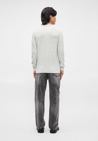 Ανοιχτό γκρι πουλόβερ από πλεκτό ύφασμα με σπογγώδη υφή, μακριά μανίκια και ριμπ ύφανση στο τελείωμα, συνδυασμένο με ξεφτισμένα μαύρα τζιν και μαύρα παπούτσια.