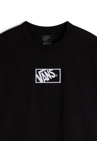 Camiseta de algodón negra con cuello redondo, que presenta un logo rectangular blanco bordado de Vans en el pecho, diseño de corte suelto.