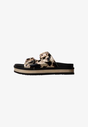 Sandalia de plataforma con tiras de estampado de vaca en negro y beige y hebillas doradas, plantilla negra y suela beige y negra.